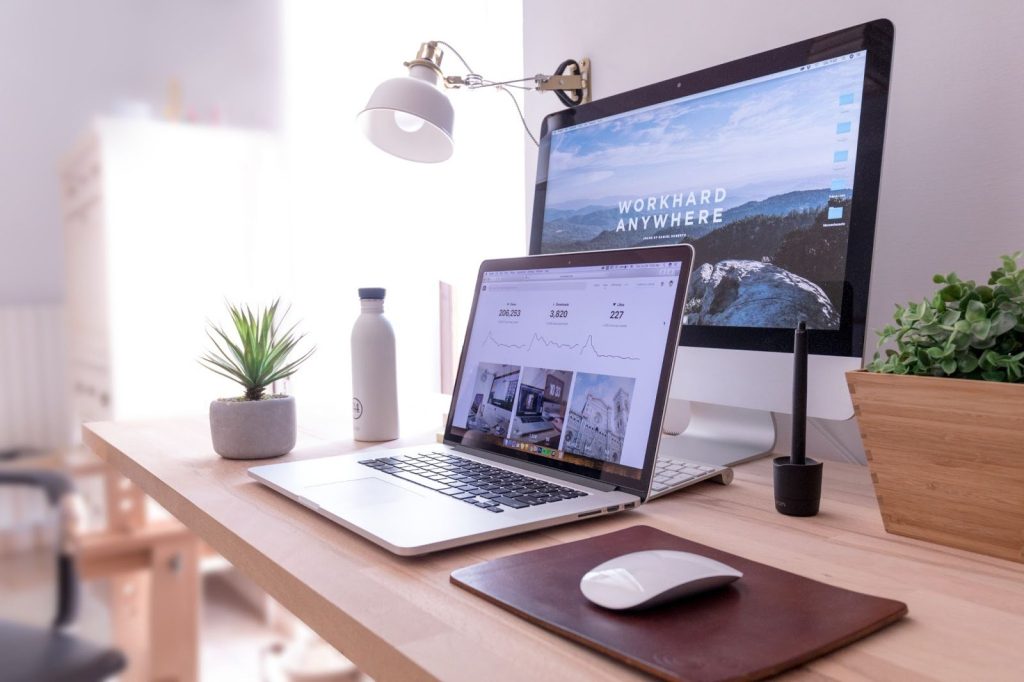 <Laptop and monitor on a wood slimline desk with two plants and a waterbottle>